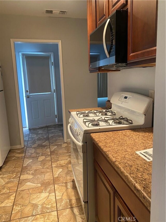 kitchen with visible vents, refrigerator, stone finish flooring, and gas range gas stove