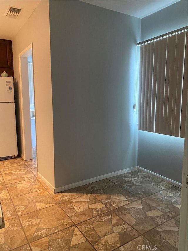 empty room featuring stone tile floors, baseboards, and visible vents