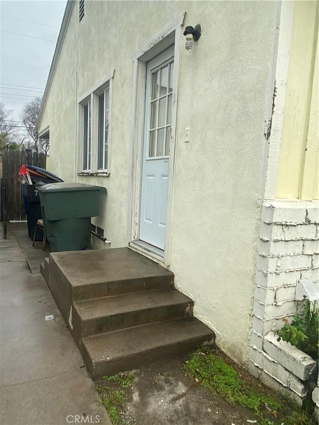 doorway to property featuring stucco siding and fence