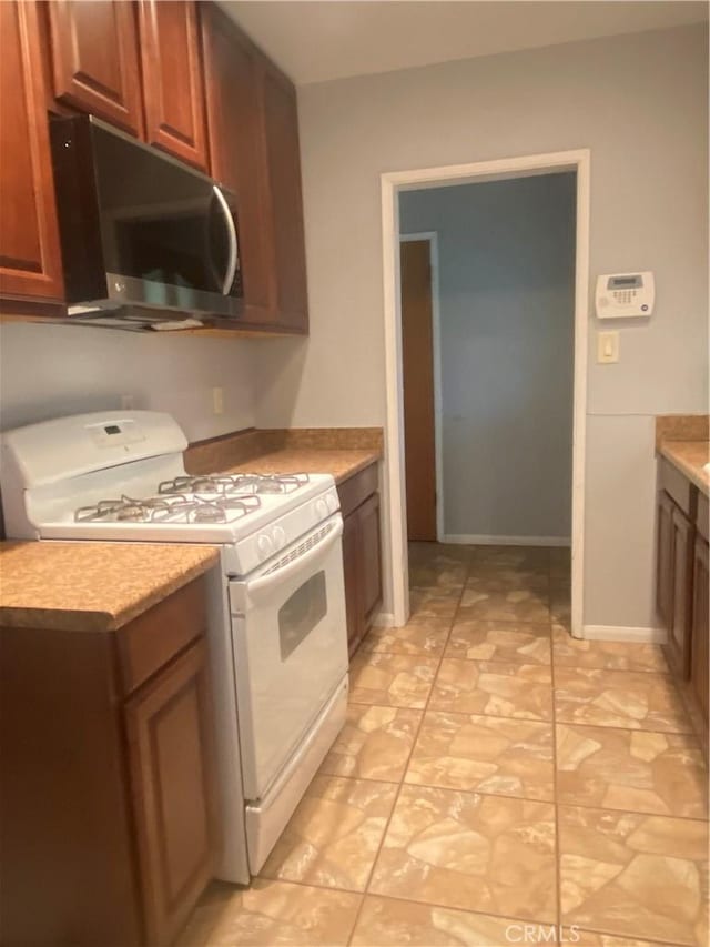 kitchen featuring baseboards, white gas range oven, and light countertops