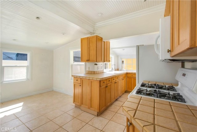 kitchen featuring tile countertops, plenty of natural light, a sink, stove, and crown molding