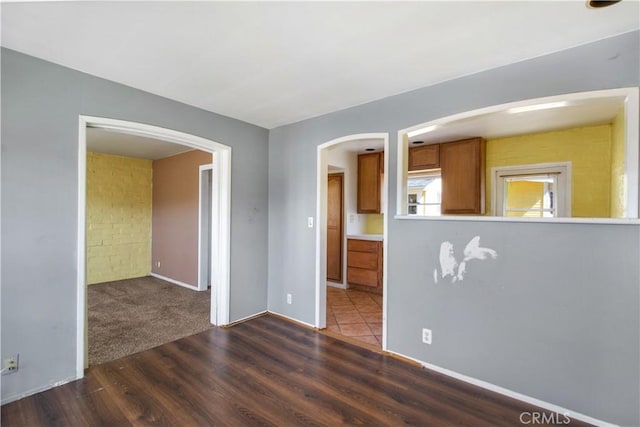 unfurnished room featuring baseboards, arched walkways, and wood finished floors