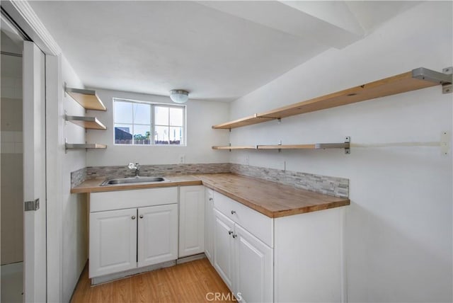 kitchen featuring open shelves, butcher block counters, light wood-type flooring, white cabinetry, and a sink