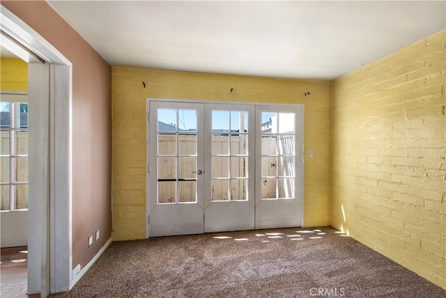 carpeted empty room featuring a healthy amount of sunlight, brick wall, and french doors