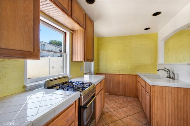 kitchen featuring a wainscoted wall, a sink, tile countertops, light tile patterned floors, and gas range