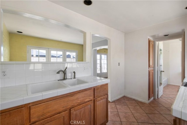 kitchen featuring tile countertops, light tile patterned floors, arched walkways, a sink, and decorative backsplash