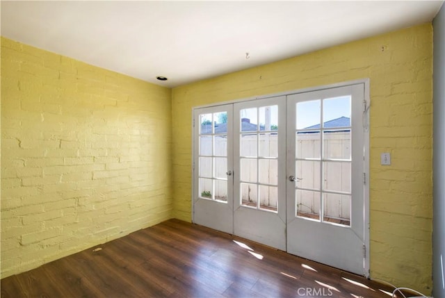 entryway with brick wall, french doors, and wood finished floors