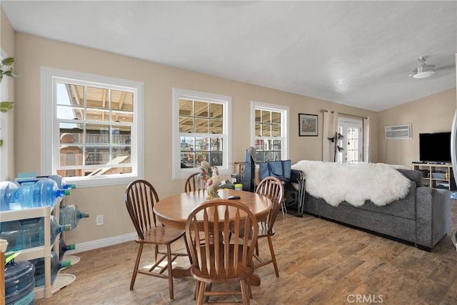 dining space featuring a wall unit AC, baseboards, lofted ceiling, and wood finished floors