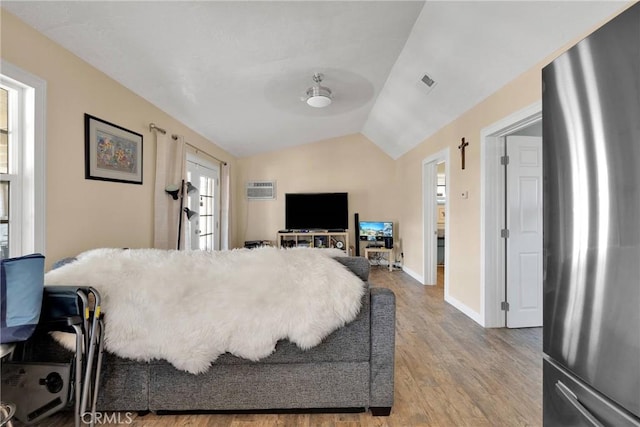 bedroom featuring visible vents, lofted ceiling, freestanding refrigerator, wood finished floors, and a wall mounted AC