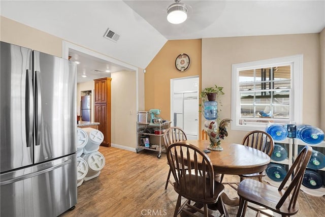 dining area featuring visible vents, baseboards, light wood-style floors, and lofted ceiling