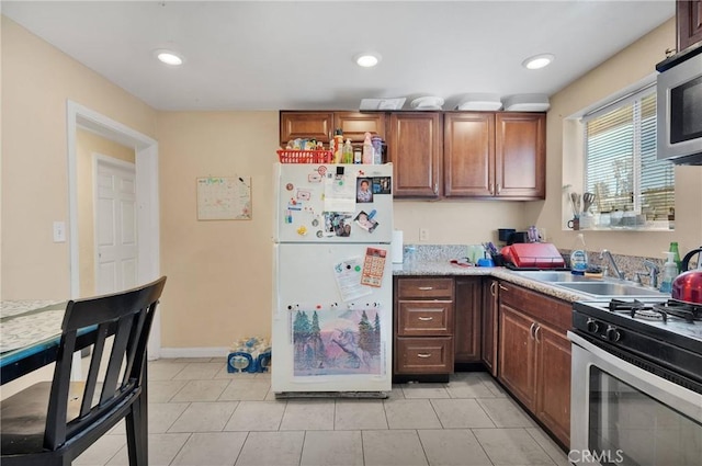 kitchen with light tile patterned floors, freestanding refrigerator, a sink, light countertops, and stainless steel gas stove