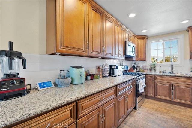 kitchen with light stone countertops, light wood-style flooring, appliances with stainless steel finishes, brown cabinetry, and a sink