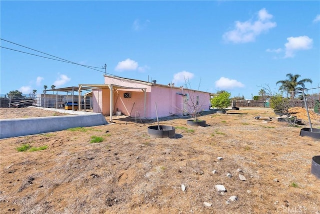 rear view of property featuring stucco siding, an outdoor structure, and fence