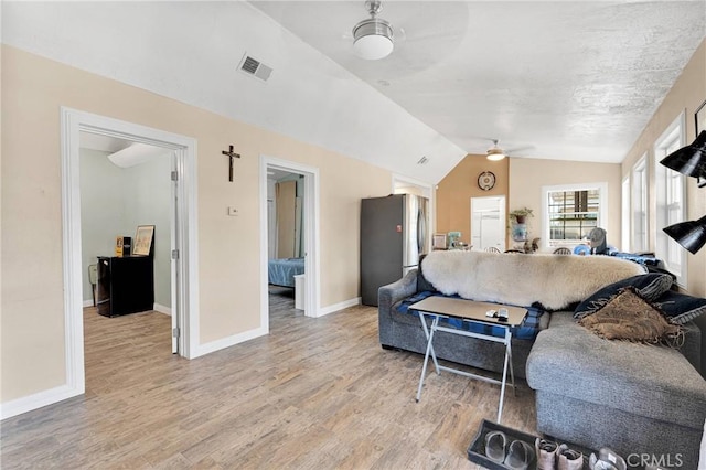 living room featuring a ceiling fan, visible vents, light wood finished floors, baseboards, and lofted ceiling