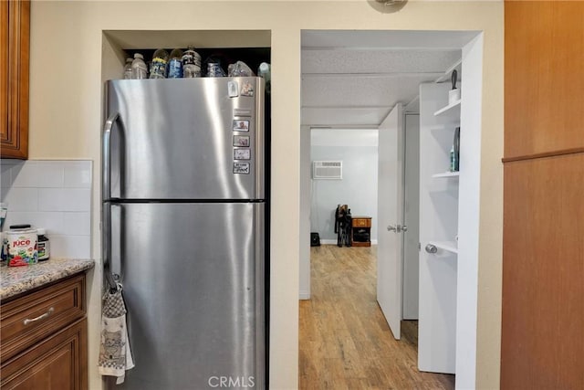 kitchen featuring tasteful backsplash, an AC wall unit, light wood-type flooring, brown cabinets, and freestanding refrigerator