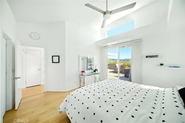 bedroom with a high ceiling, light wood-style flooring, a ceiling fan, and access to outside