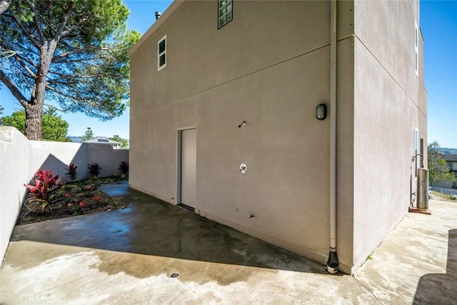 view of side of property featuring stucco siding, a patio, and fence