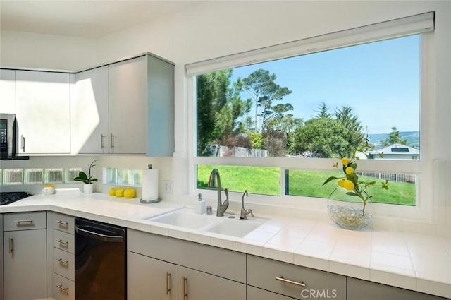 kitchen featuring dishwasher, plenty of natural light, a sink, and gray cabinetry