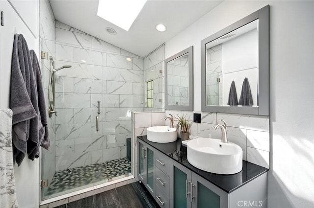 full bath with backsplash, vaulted ceiling with skylight, a shower stall, and a sink