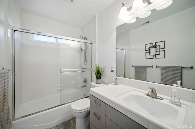 bathroom featuring visible vents, toilet, wood finished floors, shower / bath combination with glass door, and vanity