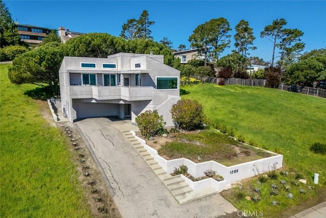 view of front of property featuring stucco siding, aphalt driveway, fence, an attached garage, and a front yard