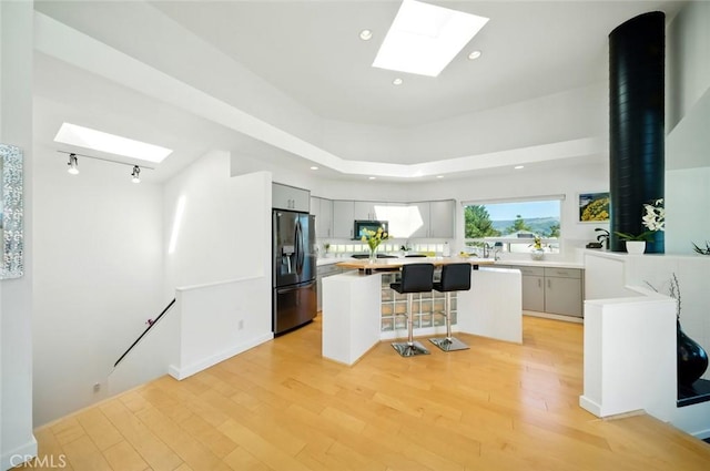 kitchen with a breakfast bar, a skylight, light wood-type flooring, and black refrigerator with ice dispenser