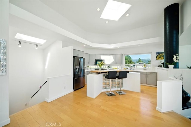1735 Spencer St, Cambria, CA 93428 - kitchen featuring black refrigerator with ice dispenser, a skylight, a breakfast bar, a center island, and light wood-style flooring