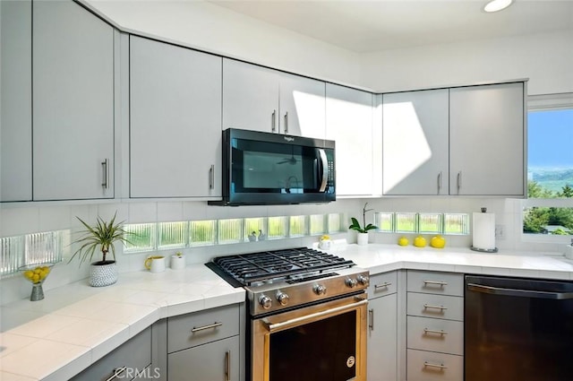 kitchen featuring dishwasher, tasteful backsplash, gray cabinets, and stainless steel gas range