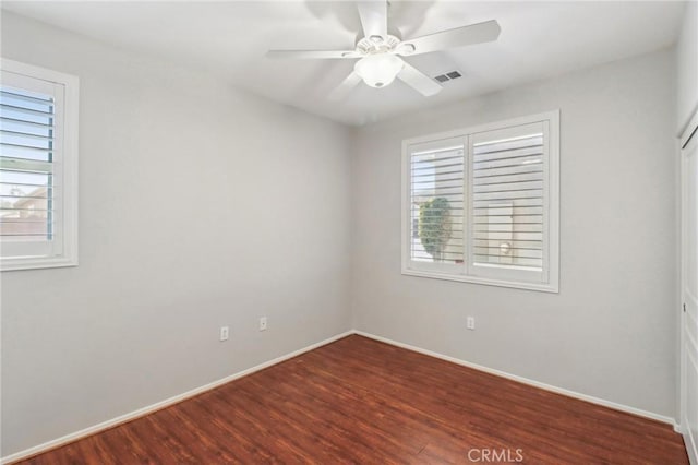 empty room featuring a ceiling fan, plenty of natural light, wood finished floors, and visible vents