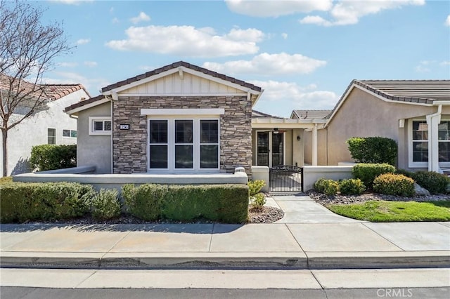 view of front of house with stucco siding, a gate, a fenced front yard, stone siding, and a tiled roof