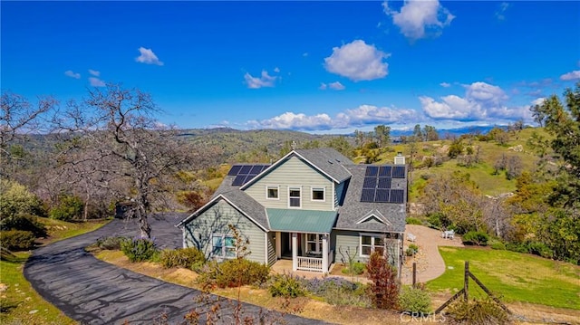 view of front of property featuring a front lawn, roof mounted solar panels, covered porch, a chimney, and metal roof