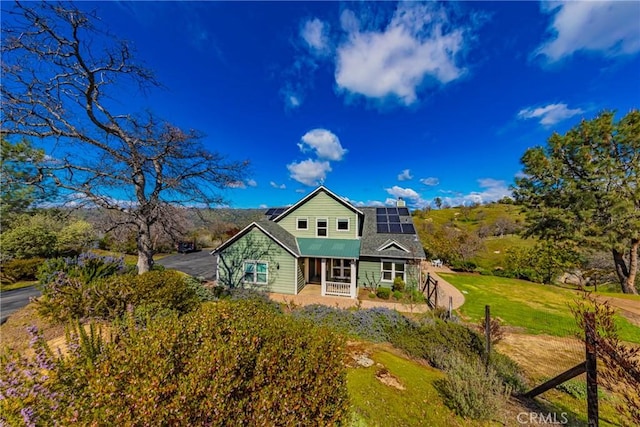 view of front of home featuring roof mounted solar panels, covered porch, and a front yard