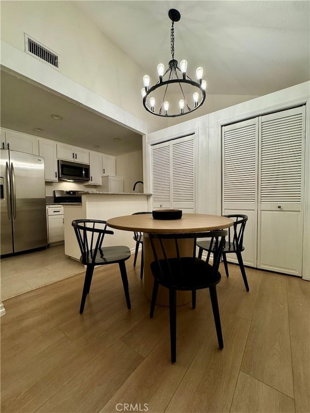 dining area featuring visible vents, light wood-type flooring, and vaulted ceiling