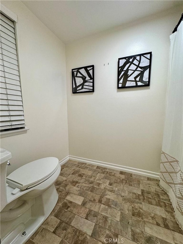 bathroom featuring curtained shower, baseboards, toilet, and stone finish floor