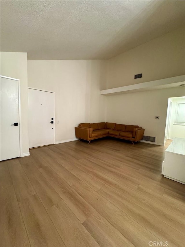 unfurnished living room featuring visible vents, a textured ceiling, and wood finished floors