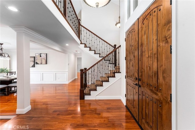 entryway with stairway, wood finished floors, a towering ceiling, and ornamental molding