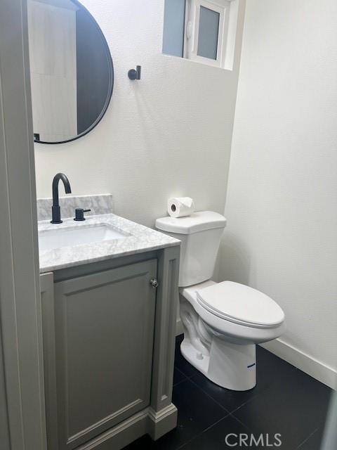 half bath featuring tile patterned floors, toilet, vanity, and baseboards