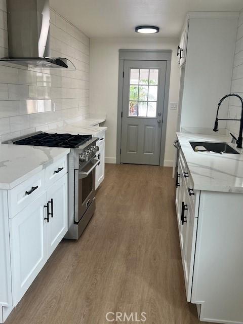 kitchen with light stone counters, wood finished floors, a sink, high end stainless steel range, and wall chimney range hood