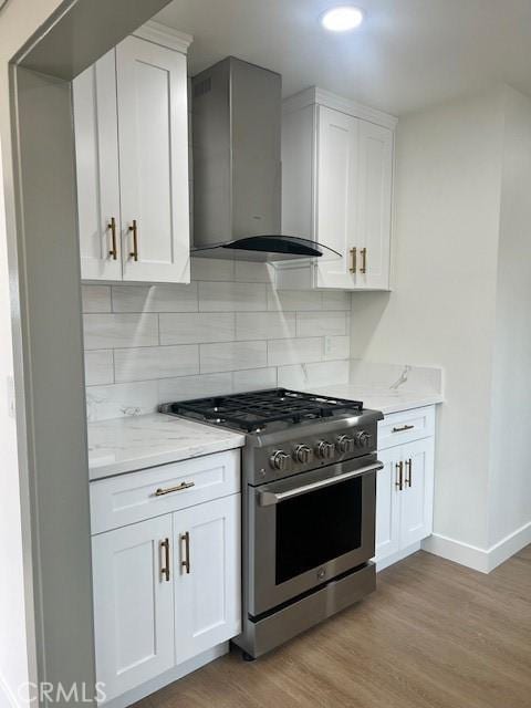 kitchen with light wood finished floors, wall chimney range hood, light stone counters, decorative backsplash, and high end range