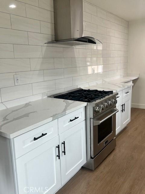 kitchen featuring high end range, light stone counters, wood finished floors, wall chimney exhaust hood, and backsplash