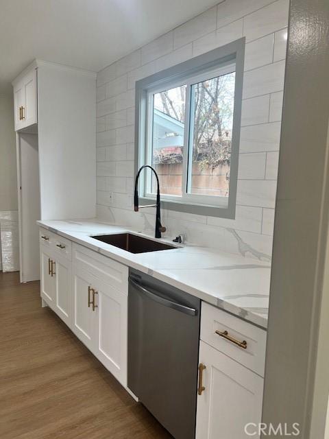 kitchen featuring backsplash, dishwasher, light wood-type flooring, light stone counters, and a sink