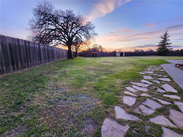 yard at dusk featuring an outbuilding, a storage unit, and a fenced backyard