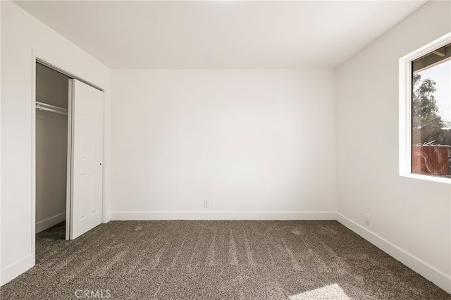 unfurnished bedroom with baseboards, dark colored carpet, and a closet