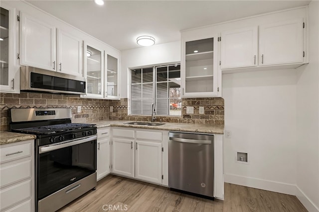 kitchen with baseboards, stainless steel appliances, light wood-style floors, white cabinetry, and a sink