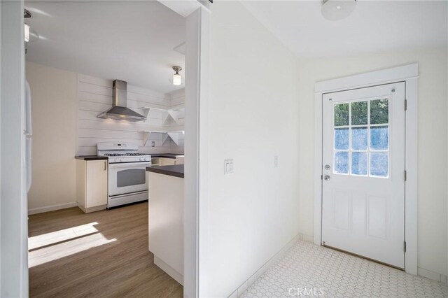 kitchen featuring baseboards, light wood-style floors, white gas range oven, dark countertops, and wall chimney range hood