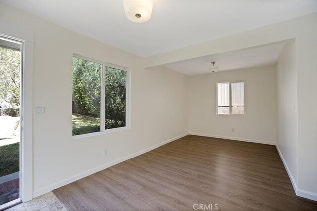 empty room with plenty of natural light, wood finished floors, and baseboards