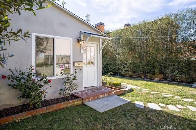 view of exterior entry featuring a chimney, stucco siding, and a lawn