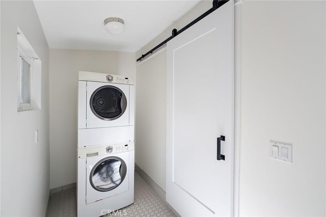 laundry area with laundry area, baseboards, a barn door, and stacked washer and dryer