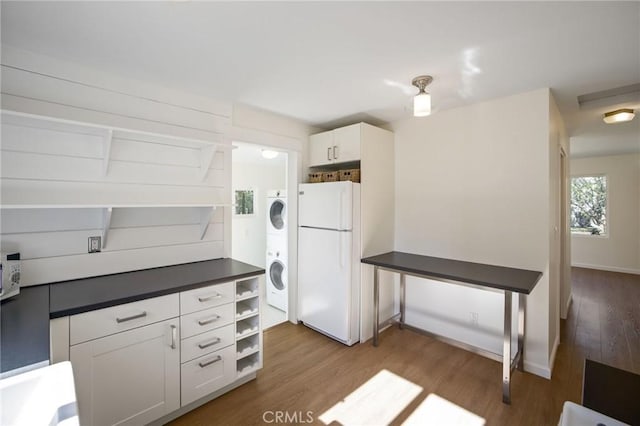 kitchen featuring open shelves, wood finished floors, stacked washer / drying machine, and freestanding refrigerator