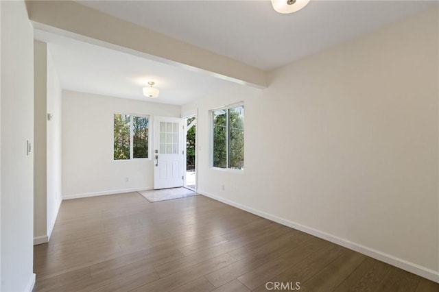 empty room with beamed ceiling, wood finished floors, and baseboards